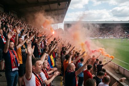 Supporters brandissant des fumigènes colorés dans les tribunes d'un stade de football lors d'un match animé