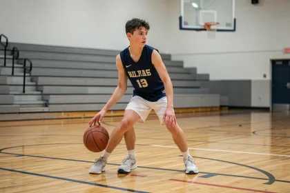 Joueur de basket scolaire en train de dribbler sur un terrain de gymnase intérieur lors d'un match officiel